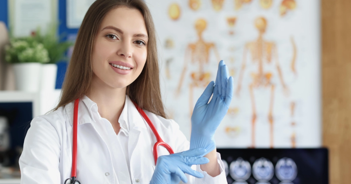Smiling female plastic surgeon in Stuart, FL, wearing a white coat and putting on blue surgical gloves.